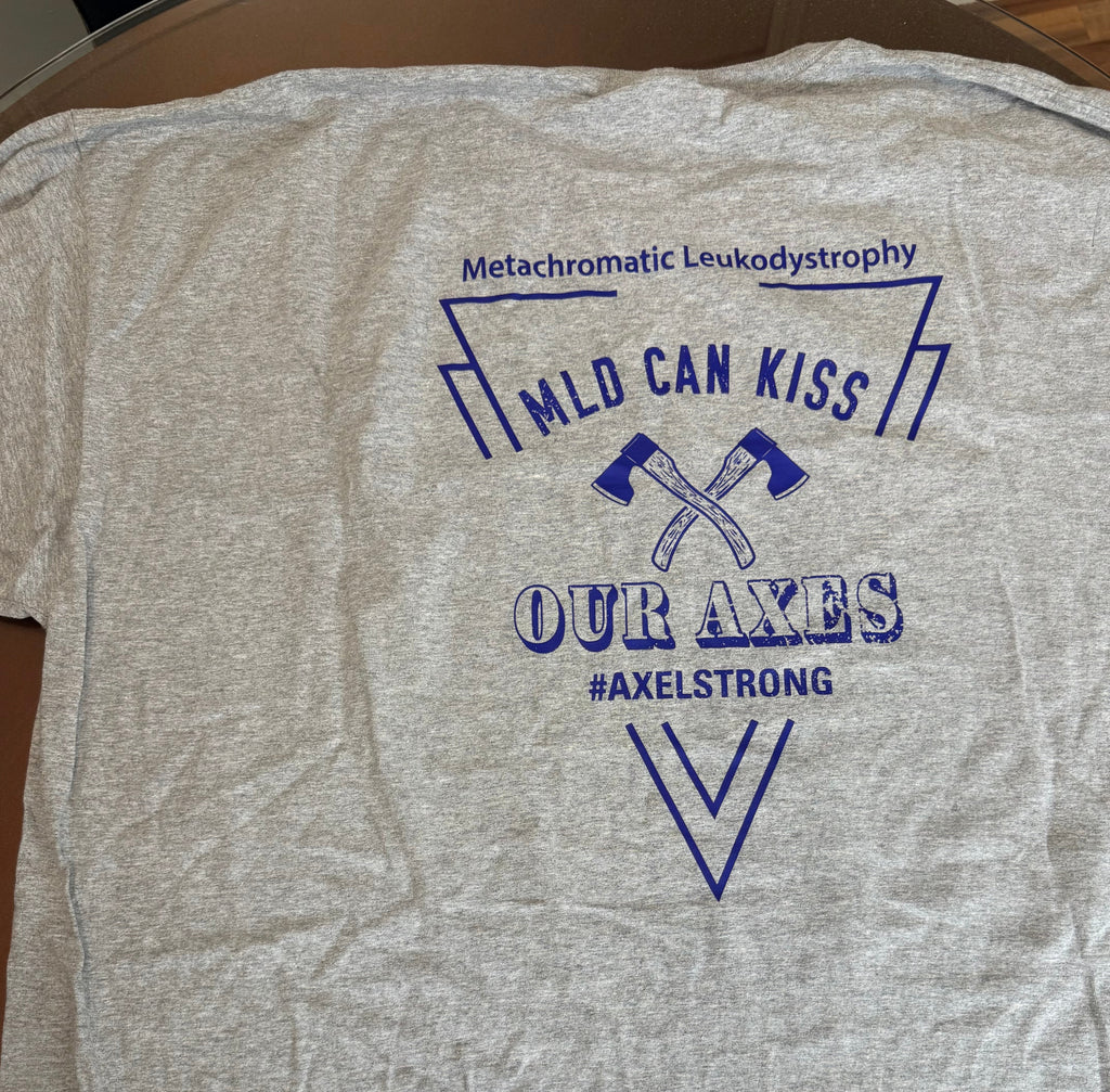 A heather gray short-sleeve t-shirt laid flat, featuring a blue graphic print on the front that reads 'Metachromatic Leukodystrophy', 'MILD CAN KISS', 'OUR AXES', and '#AXELSTRONG' with crossed axes. Two small handwritten size tags reading 'SHORT SLEEVE' and '3YL' are placed near the bottom.