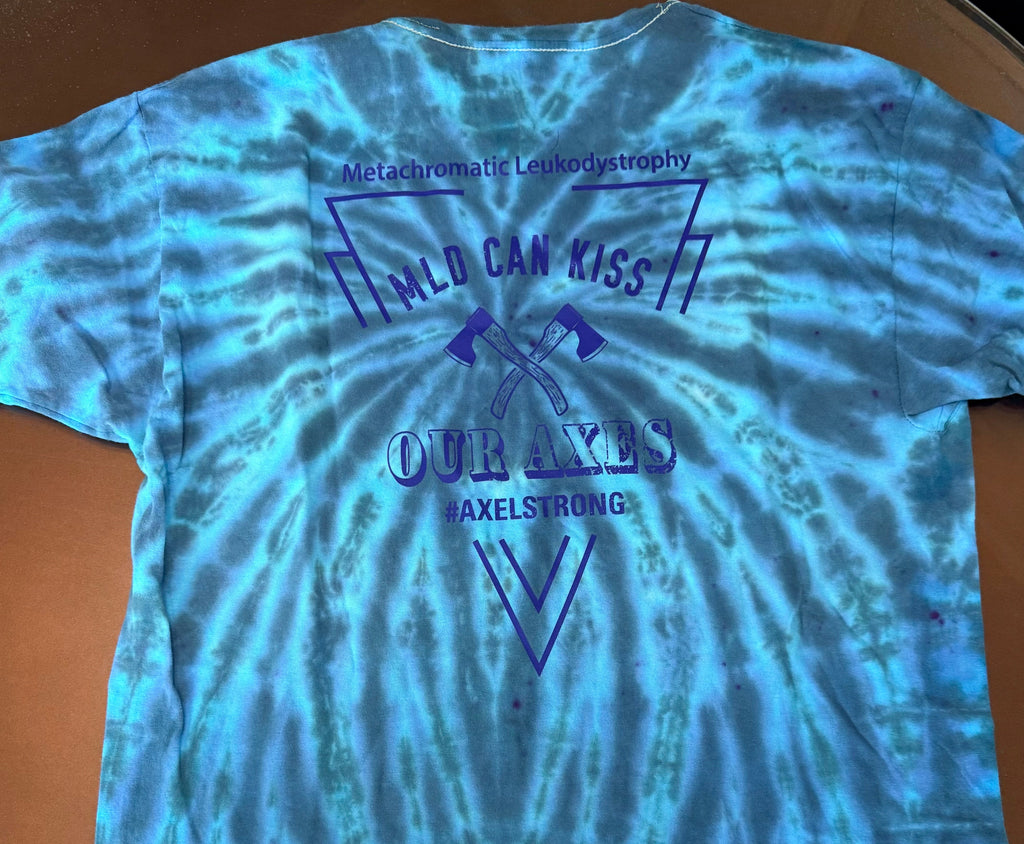 A blue and teal tie-dye t-shirt laid flat on a brown surface, featuring a dark blue graphic print on the back with the words 'World Can Kiss Our Axes' and 'Axelstrong'. 