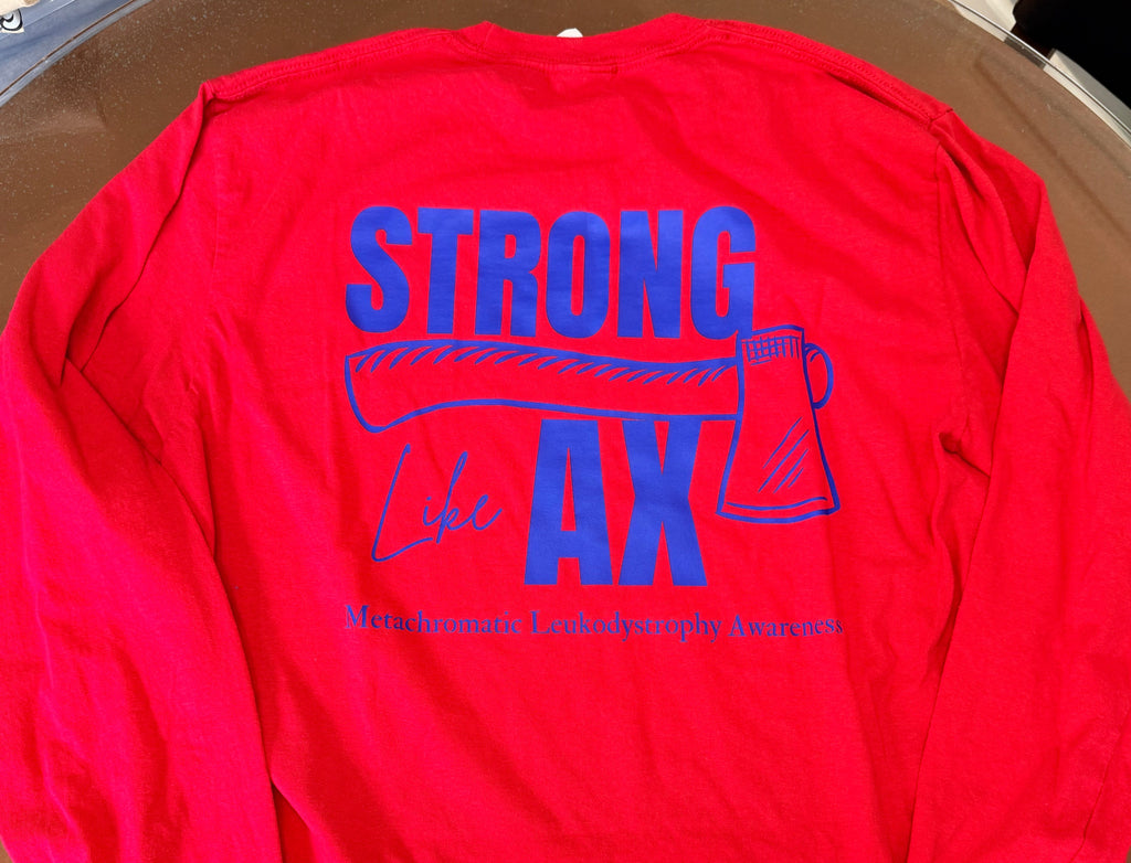 A bright red long-sleeve shirt laid flat on a brown wooden table, showing the back with a large blue graphic that reads 'STRONG like AX' and smaller text below. 