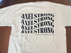 A cream-colored short-sleeve t-shirt laid flat on a brown glass table, featuring the word 'AXELSTRONG' repeated in a wavy black font across the chest. 