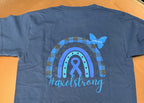 A blue short-sleeve T-shirt laid flat on an orange surface, showing the back with a large rainbow and awareness ribbon graphic in blue and gray, plus the text '#axelstrong'. 